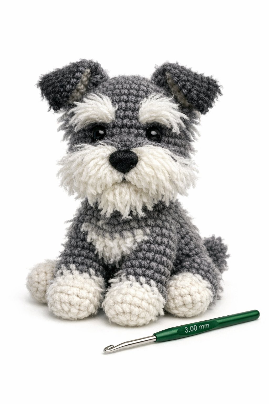 A crocheted schnauzer dog with fluffy fur sitting upright next to a crochet hook.